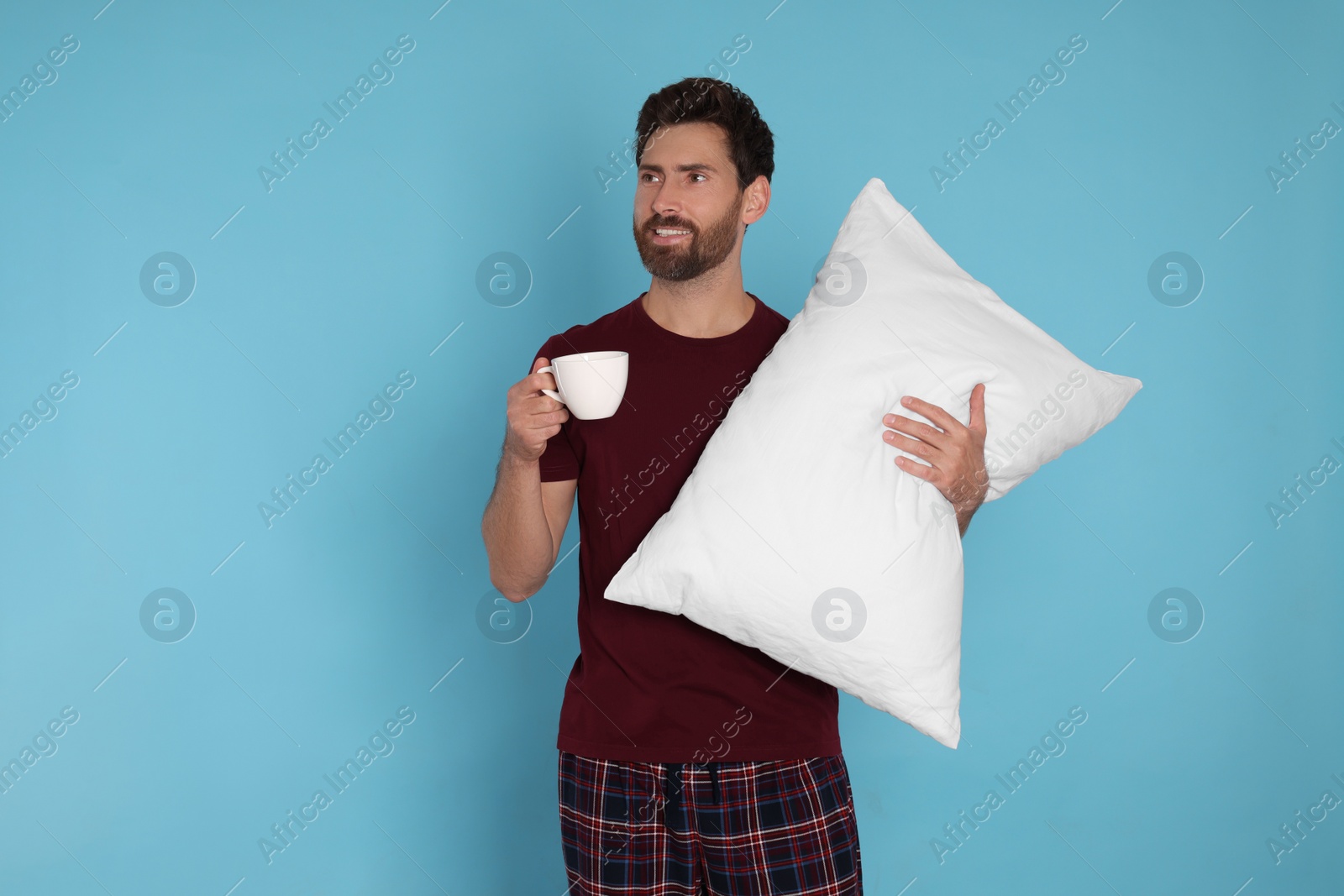 Photo of Handsome man with cup of hot drink and soft pillow on light blue background