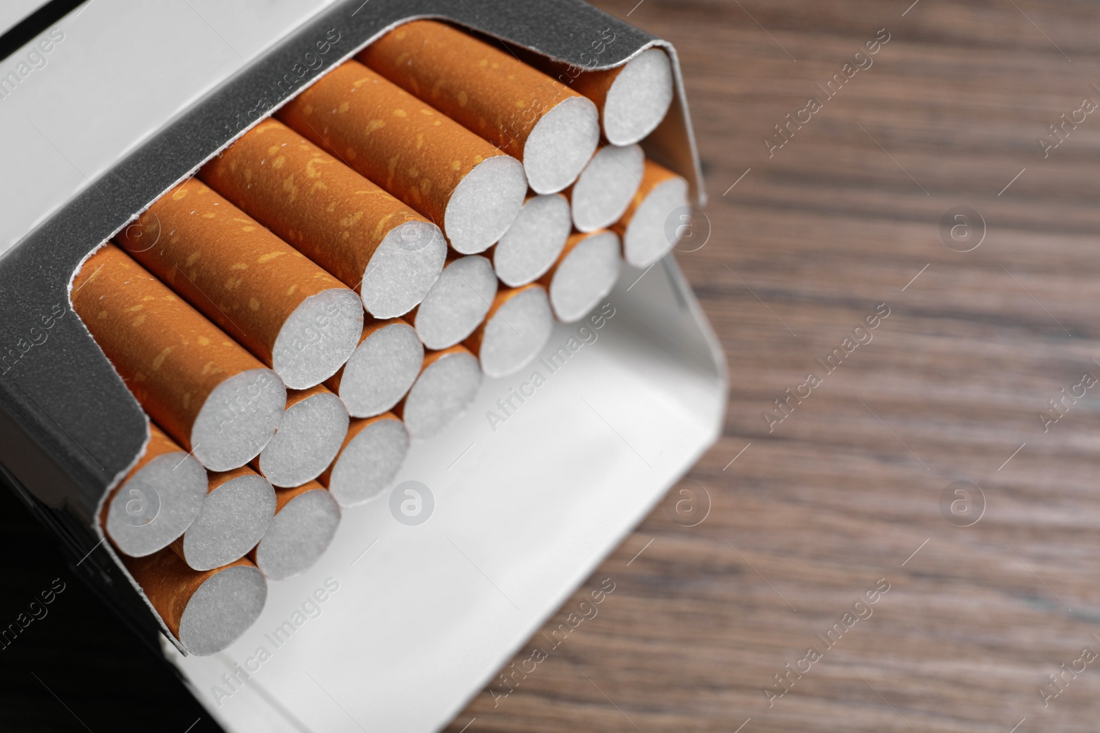 Photo of Cigarettes in pack on wooden table, closeup. Space for text