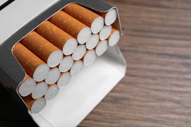 Photo of Cigarettes in pack on wooden table, closeup. Space for text