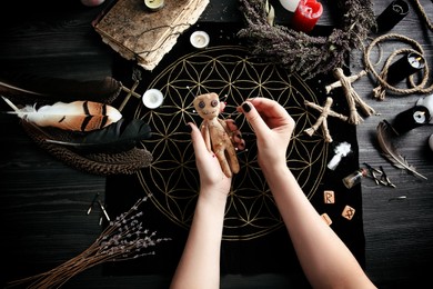 Photo of Woman stabbing voodoo doll with needle at table, closeup. Curse ceremony