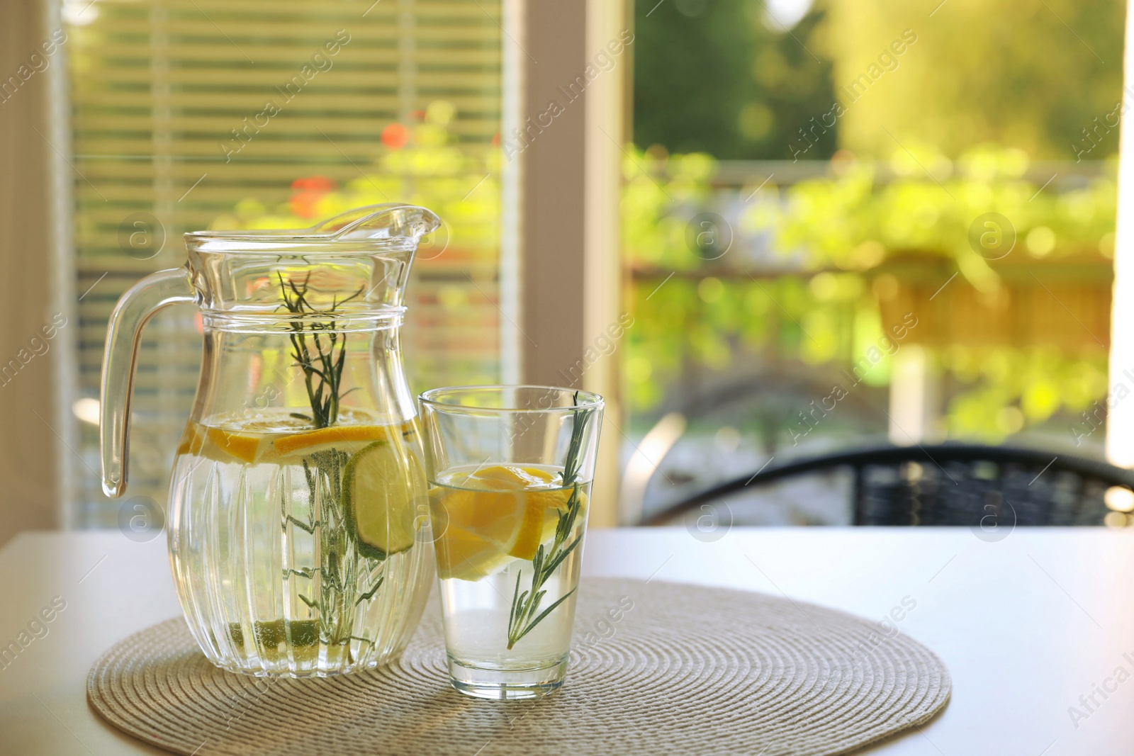 Photo of Jug and glass with refreshing lemon water on light table indoors. Space for text