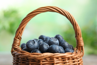 Wicker basket with fresh blueberries on blurred green background, closeup