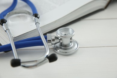 Photo of One medical stethoscope and book on white wooden table, closeup