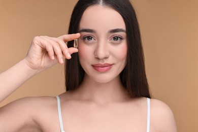 Beautiful young woman with vitamin pill on beige background