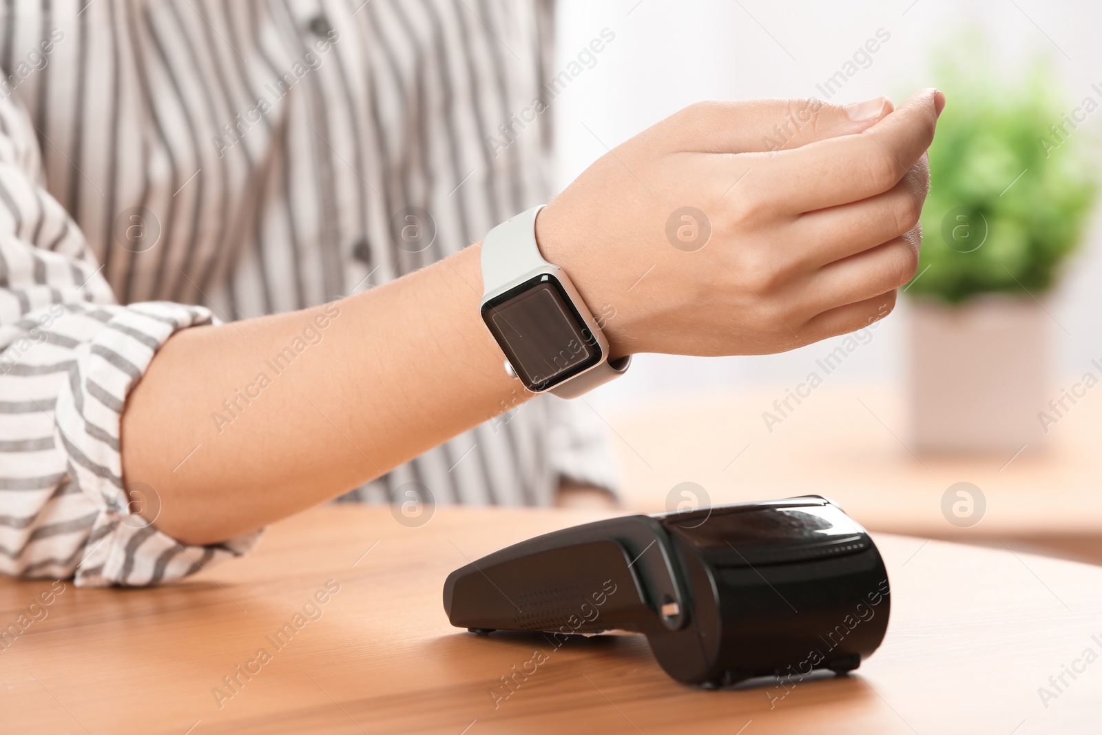 Photo of Woman using terminal for contactless payment with smart watch indoors