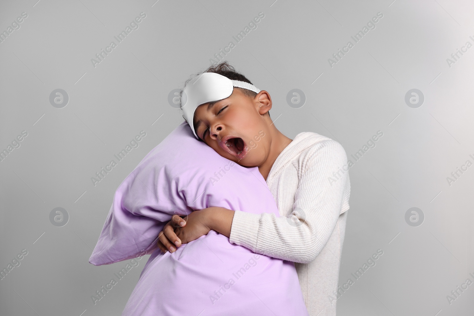 Photo of Boy with pillow and sleep mask yawning on grey background. Insomnia problem