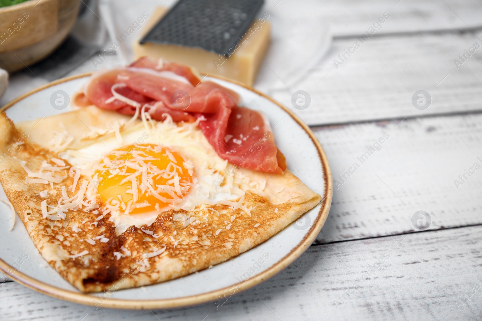 Photo of Delicious crepe with egg on white wooden table, closeup. Breton galette