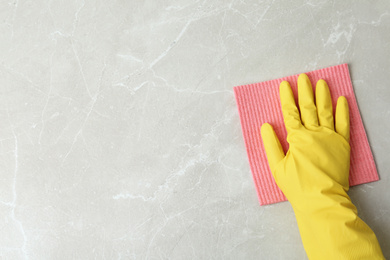 Photo of Person in gloves wiping grey marble table with rag, top view. Space for text