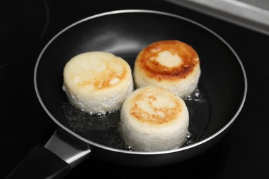 Delicious cottage cheese pancakes in frying pan on cooktop