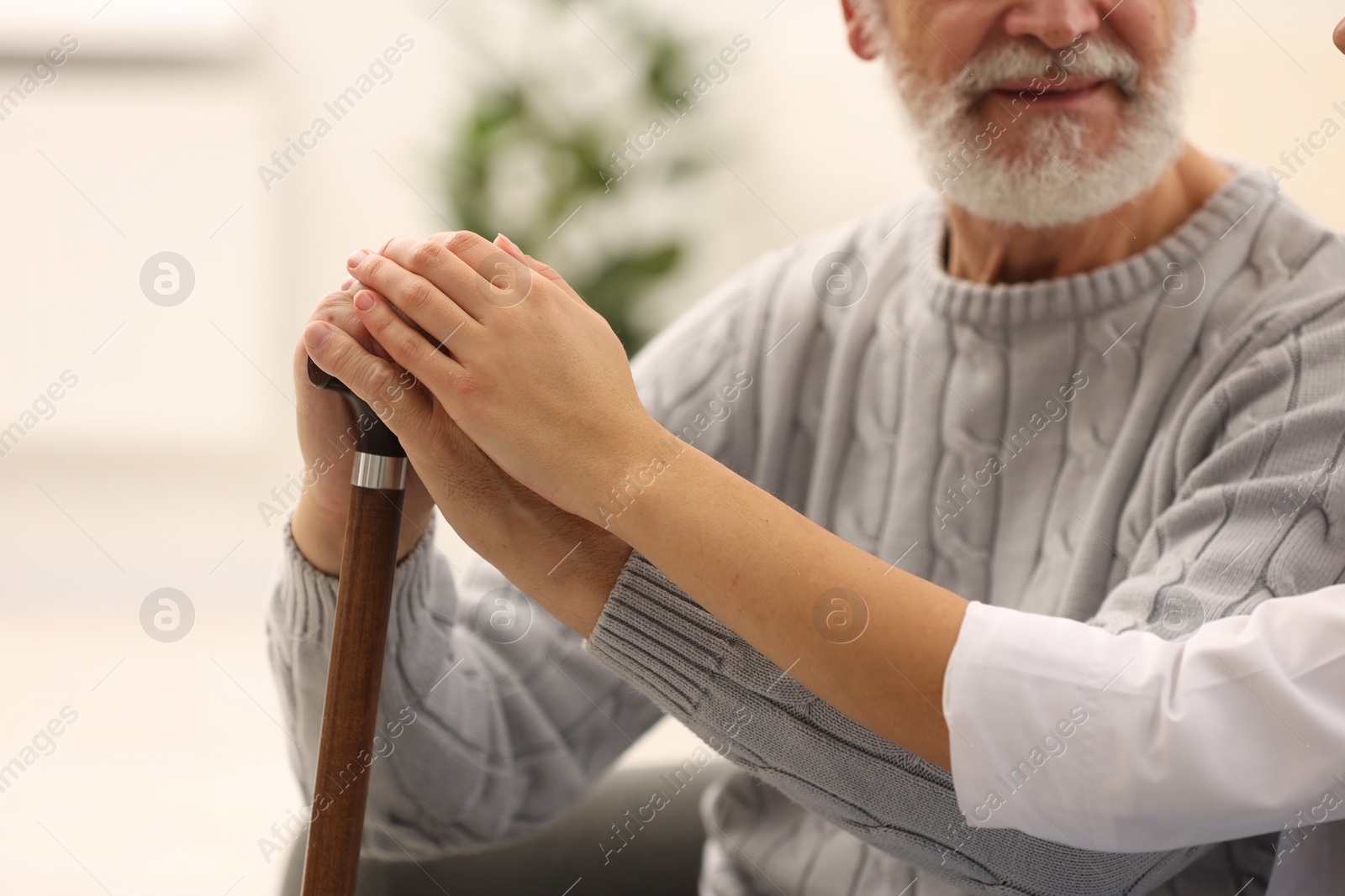 Photo of Nurse supporting elderly patient indoors, closeup view