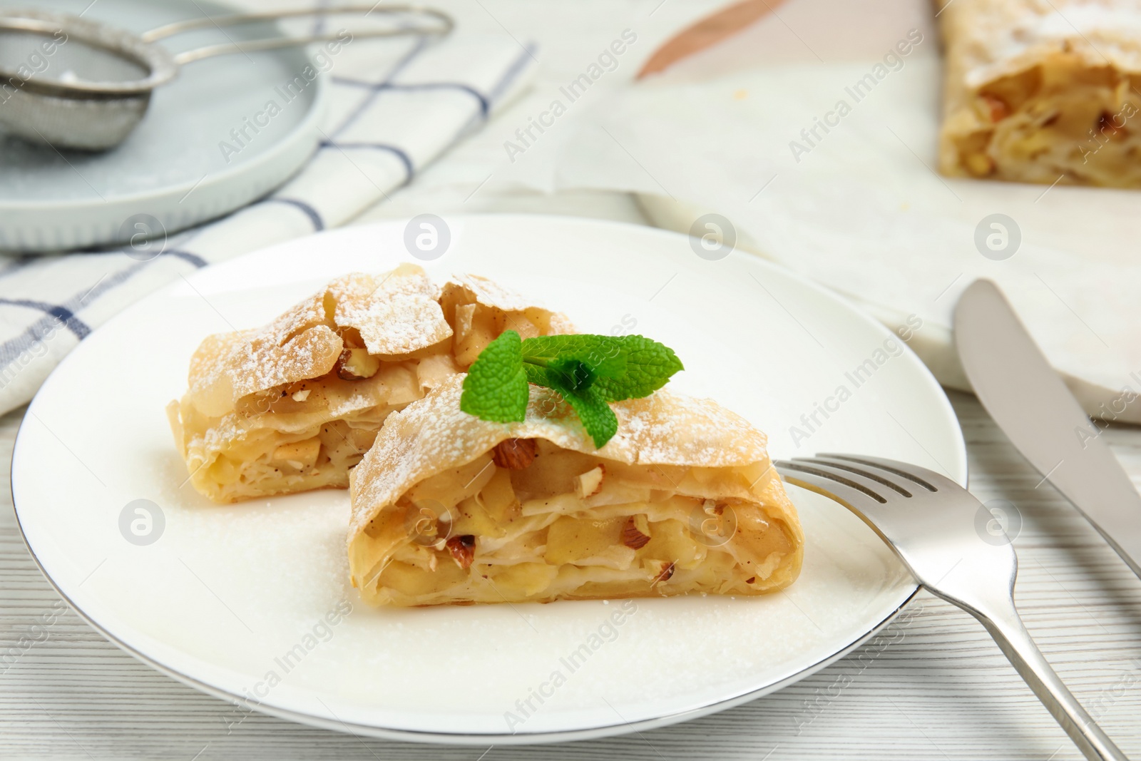 Photo of Pieces of delicious apple strudel with almonds, powdered sugar and mint on white wooden table