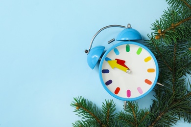 Alarm clock and fir branches on light blue background, flat lay with space for text. New Year countdown