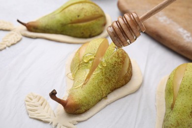 Photo of Pouring honey onto raw dough with fresh pears on table, closeup