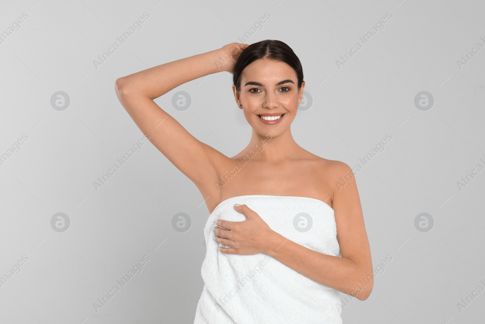 Photo of Young woman showing hairless armpit after epilation procedure on light grey background