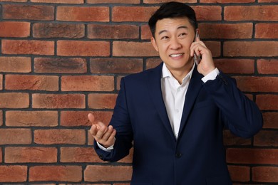 Photo of Happy boss talking on phone near brick wall. Space for text