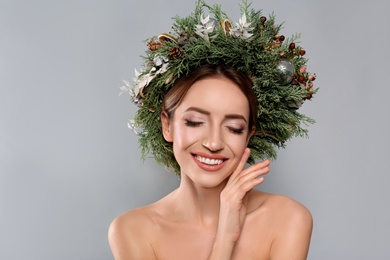 Beautiful young woman wearing Christmas wreath on grey background