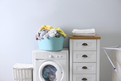 Photo of Plastic basket with dirty laundry on washing machine indoors