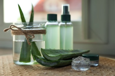 Photo of Green aloe vera leaves and cosmetic products on table near window indoors