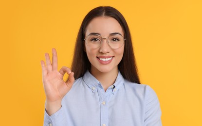 Beautiful woman in glasses showing OK gesture on orange background