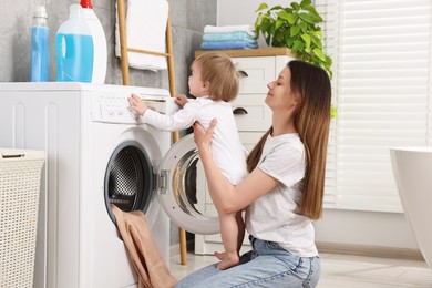 Mother with her daughter washing baby clothes in bathroom