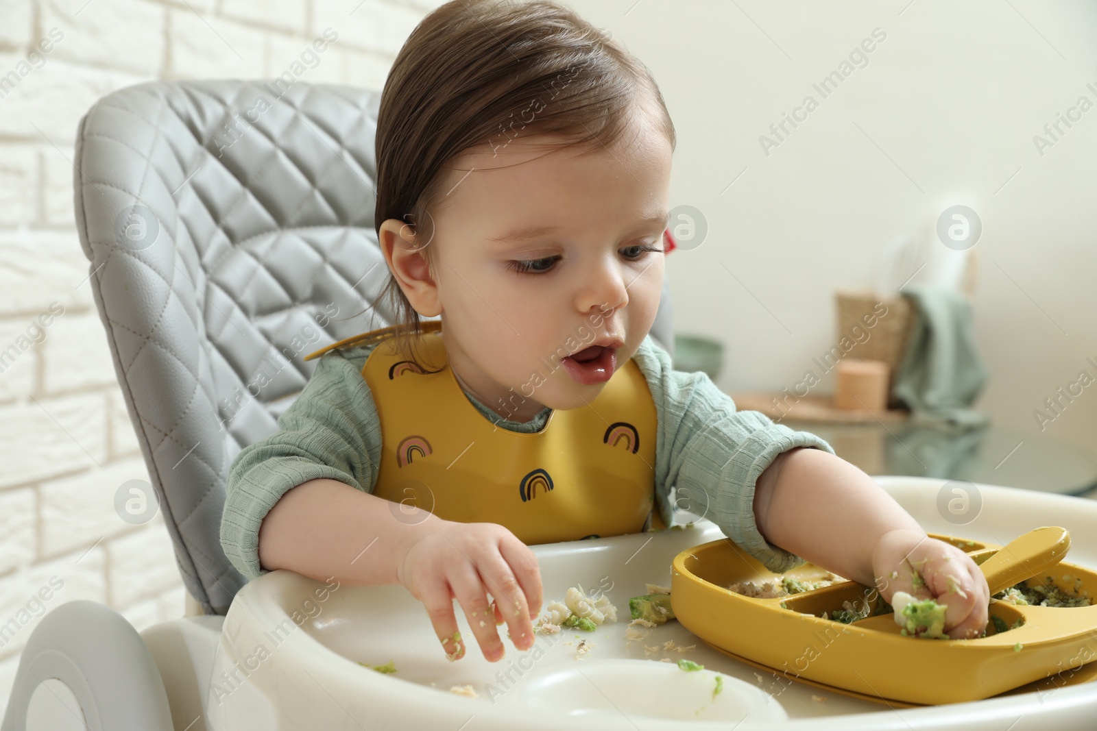 Photo of Cute little baby eating healthy food in high chair indoors