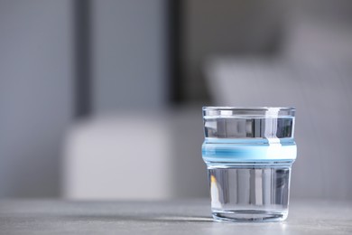 Glass of clean water on light grey table indoors, space for text
