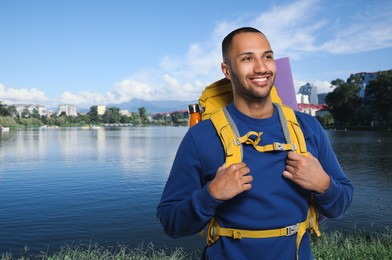 Happy tourist with yellow backpack near lake