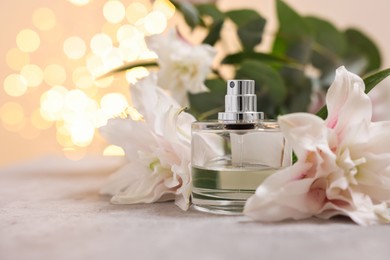 Photo of Bottle of perfume and beautiful lily flowers on table against beige background with blurred lights, closeup