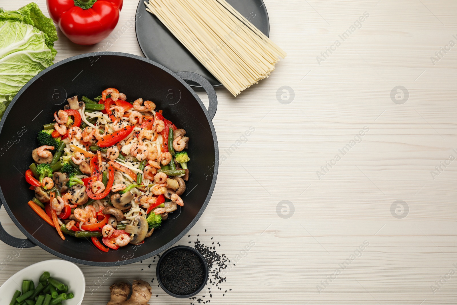 Photo of Stir fried noodles with mushrooms, shrimps and vegetables in wok on white wooden table, flat lay.  Space for text