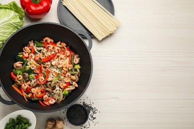 Photo of Stir fried noodles with mushrooms, shrimps and vegetables in wok on white wooden table, flat lay.  Space for text