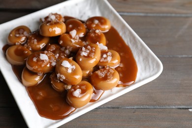 Photo of Plate with tasty candies, caramel sauce and salt on wooden table
