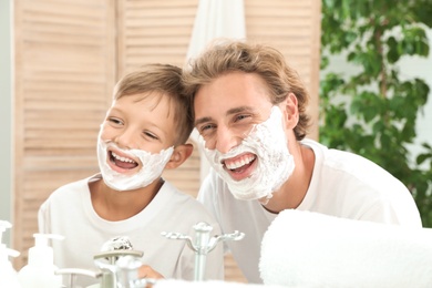 Father and son having fun with shaving foam on faces in bathroom