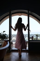 Photo of Young woman standing on balcony, back view