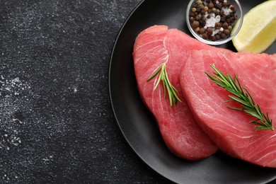 Raw tuna fillets with rosemary on black table, top view. Space for text
