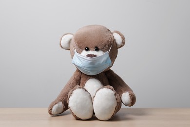 Photo of Cute teddy bear in medical mask on wooden table near light wall