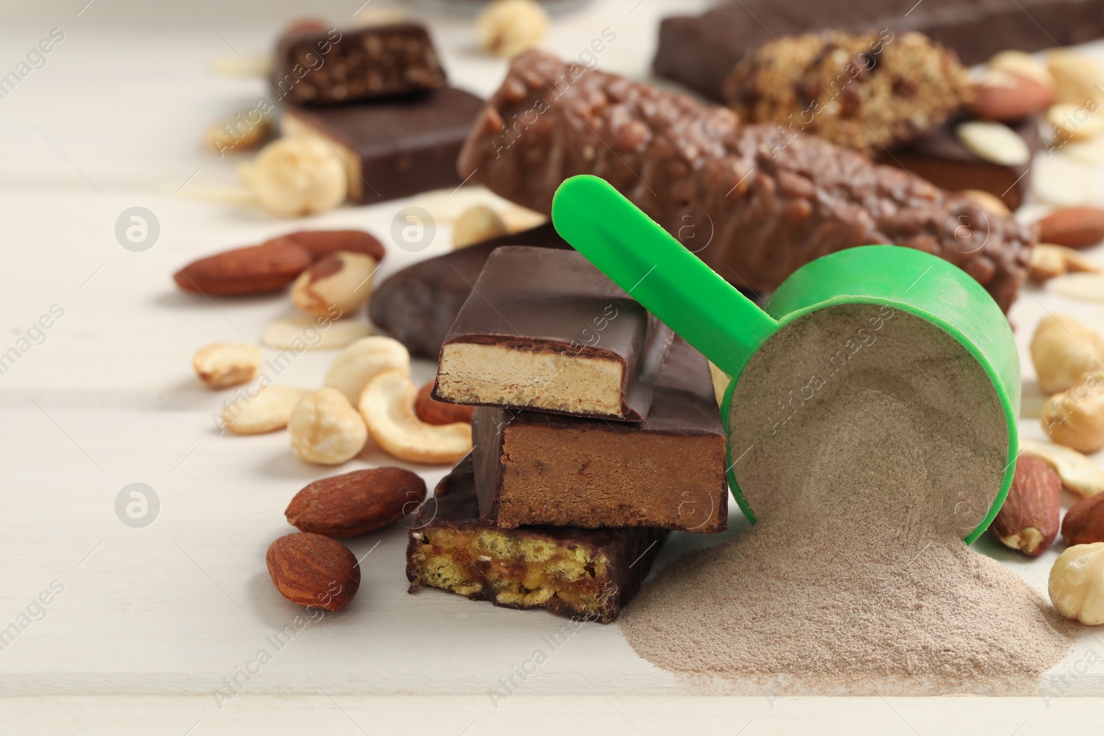 Photo of Different energy bars, nuts and protein powder on white wooden table, closeup