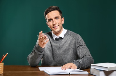 Portrait of male teacher working at table against color background