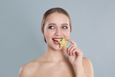 Young woman with slice of carambola on grey background. Vitamin rich food