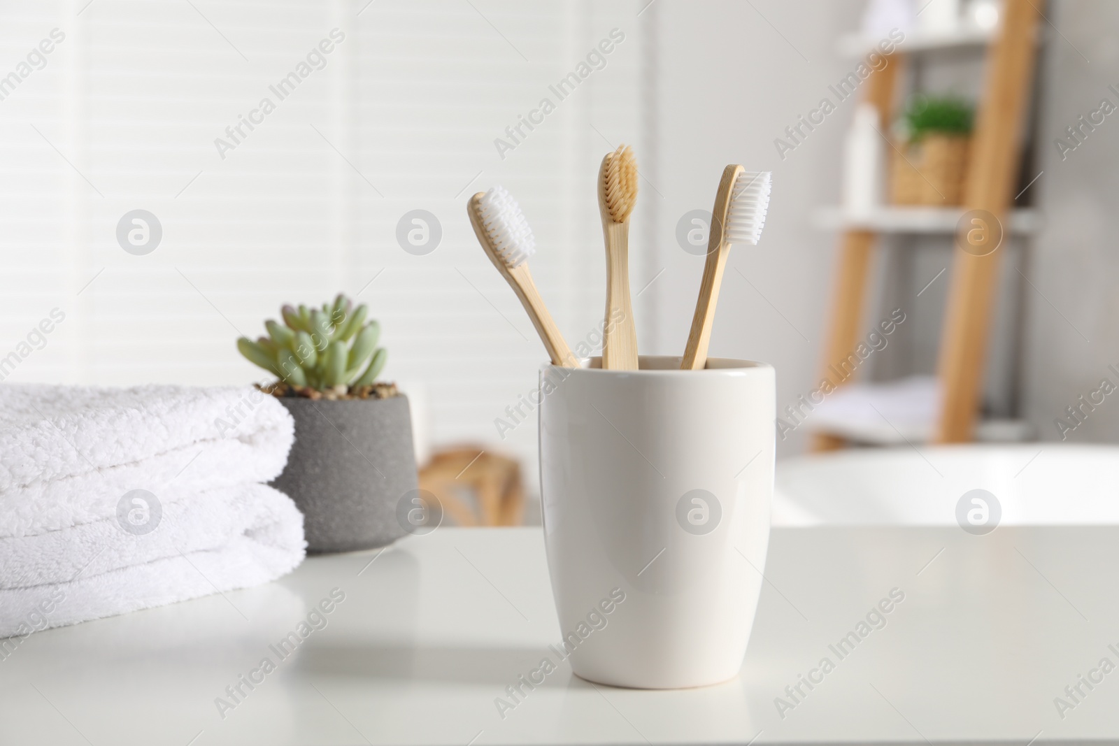 Photo of Holder with bamboo toothbrushes, potted plant and towels on white countertop in bathroom