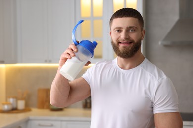 Young man with shaker of protein in kitchen, space for text