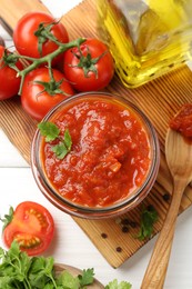 Photo of Homemade tomato sauce in jar, spoon and fresh ingredients on white wooden table, flat lay