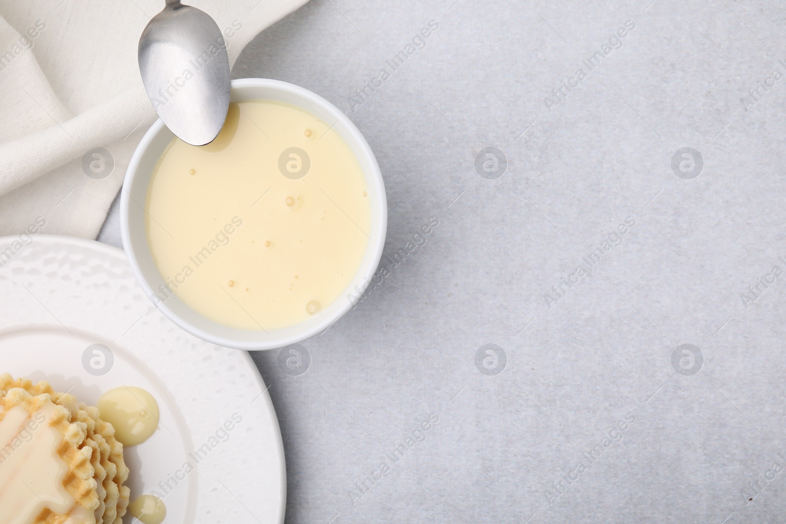 Photo of Tasty condensed milk, spoon and waffles on light grey table, flat lay. Space for text