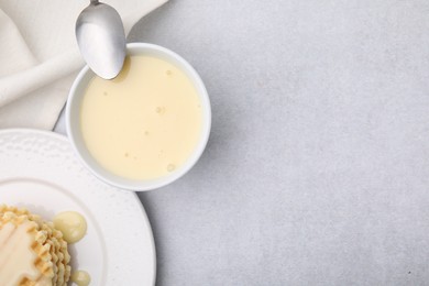 Photo of Tasty condensed milk, spoon and waffles on light grey table, flat lay. Space for text