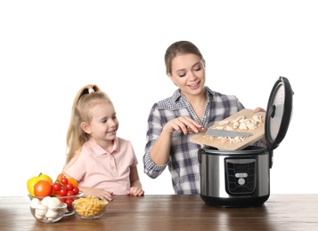 Mother and daughter preparing food with modern multi cooker at table against white background