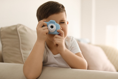 Photo of Little photographer taking picture with toy camera on sofa at home