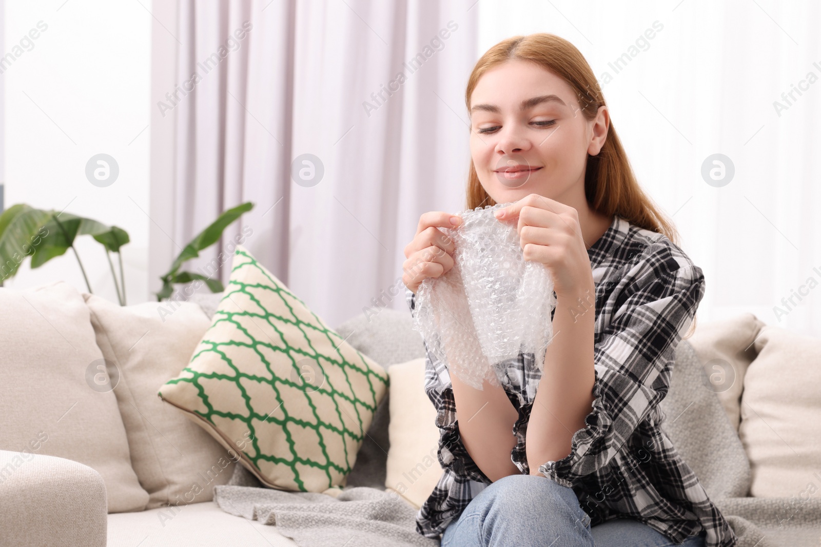 Photo of Woman popping bubble wrap on sofa at home, space for text. Stress relief