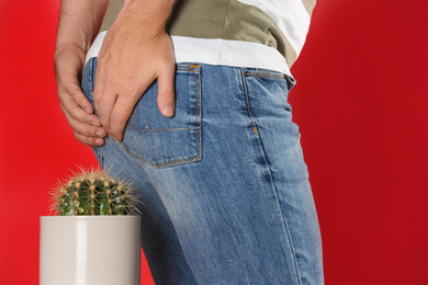 Photo of Man sitting down on cactus against red background, closeup. Hemorrhoid concept