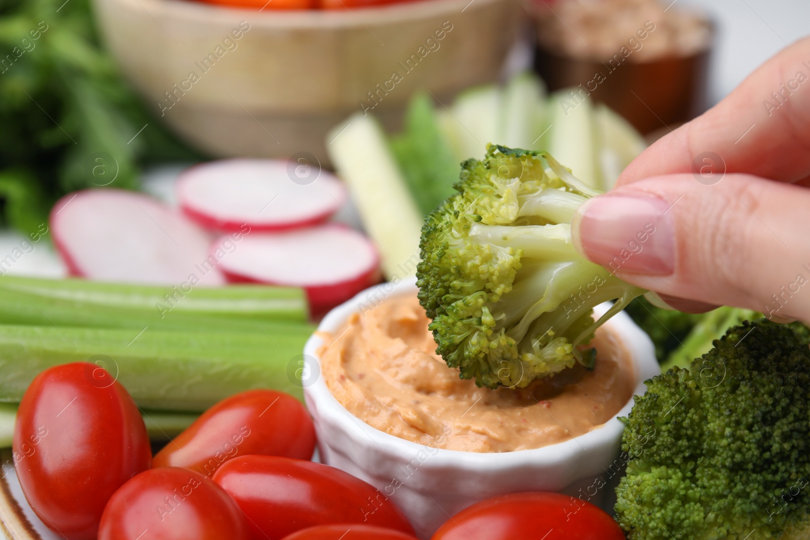 Photo of Woman dipping broccoli into hummus at table, closeup