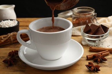 Photo of Pouring tasty hot chocolate into cup at wooden table, closeup