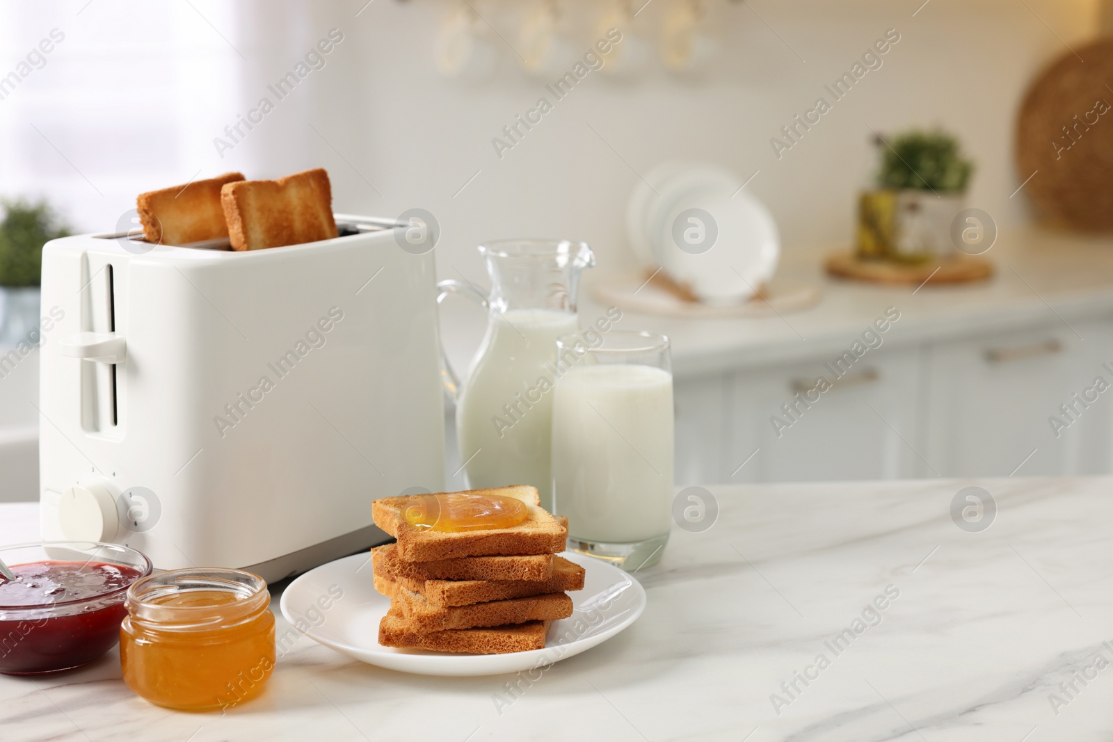 Photo of Making toasts for breakfast. Appliance, crunchy bread, honey, jam and milk on white marble table in kitchen. Space for text